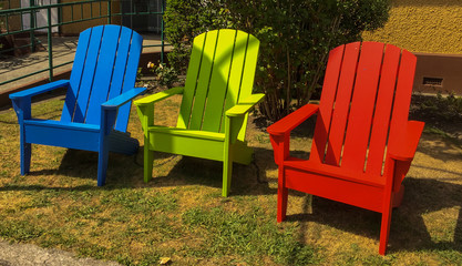 Three empty colourful wooden chairs sitting on the lawn