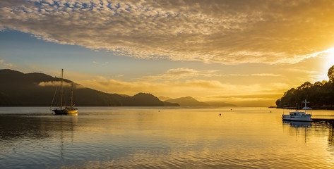A golden sunset across the Marlborough Sound, will calm waters and several boats in the foreground.