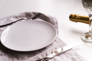 Empty plate with butter knife on napkin near champagne bottle over white background