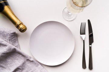 Dining table with empty plate and champagne bottle over white background