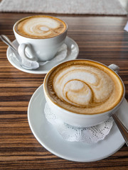 Two cup of cappuccino with latte art on wooden background. Hot coffee on table. Side view. Beautiful foam
