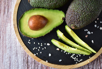 Fresh oily fruits of a young avocado on a chopping board with spices from above