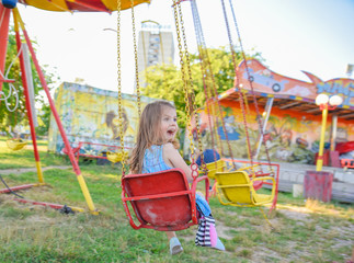Little girl screaming and shouting happily while holding firmly on the colorful merry go around in the amusement park ride during the afternoon on a summer day