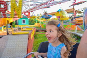 Girl screaming and shouting happily while holding firmly on the colorful carousel amusement park...
