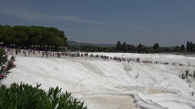 Pamukkale, Denizli, Turkey - 16th of July 2019: 4K Zoom out tourists walking on the sinter terraces