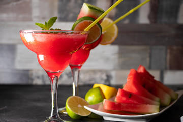 Two watermelon cocktails with slices of watermelon, lemon and lime