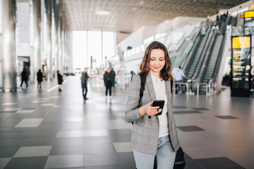 Young girl at the airport walks, looking at her smartphone, smiling.