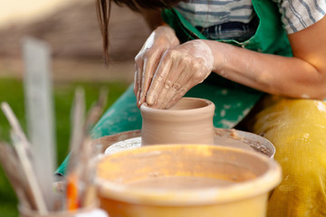 Hand craft making pottery on wheel. Female hands mold ceramic plate from clay (pot).