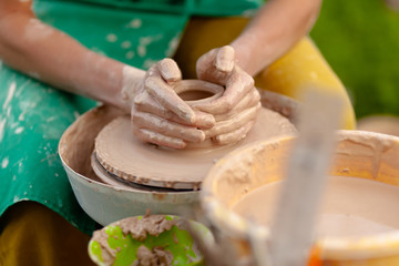 Hand craft making pottery on wheel. Female hands mold ceramic plate from clay (pot).