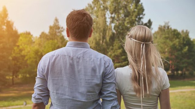 Young man and woman stand with their backs in the park