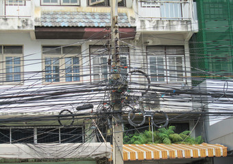 A column with a lot of wires on the background of a multi-storey building. Thailand