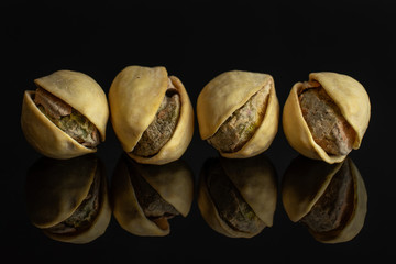 Group of four whole ripe green pistachio in closeup in row isolated on black glass