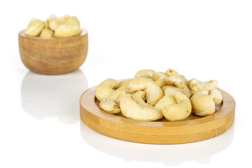 Lot of whole unsalted beige cashew on round bamboo coaster in tiny wooden bowl isolated on white background