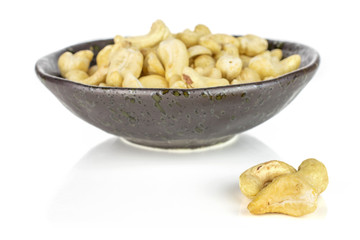 Lot of whole unsalted beige cashew in dark ceramic bowl isolated on white background