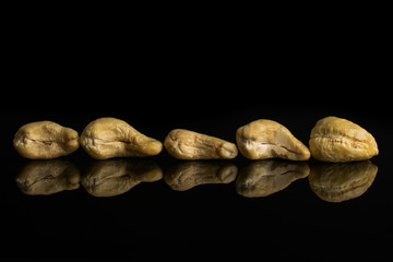Group of five whole unsalted beige cashew isolated on black glass
