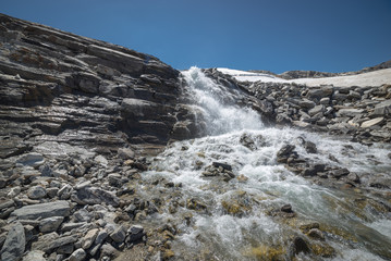Fototapeta na wymiar Waterfall and stream in a rocky and snowy alpine landscape