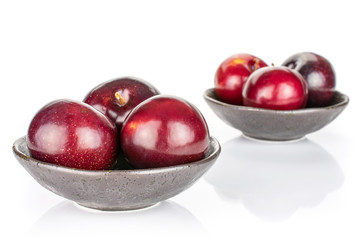 Group of six whole ripe red round plum in dark ceramic bowl isolated on white background