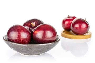 Group of five whole ripe red round plum in dark ceramic bowl on round bamboo coaster isolated on white background