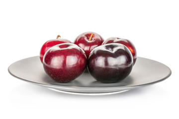 Group of five whole ripe red round plum on gray ceramic plate isolated on white background