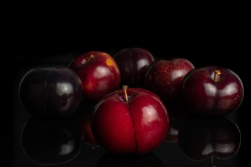 Group of six whole ripe red round plum arranged symmetrically isolated on black glass