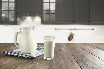 Glass of fresh milk and jug on wooden tabletop with blur kitchen as background. Space for text or display product.