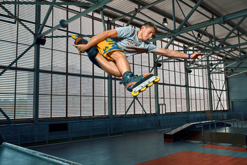 Rollerblader jump high from big air ramp performing trick. Indoors skate park equipment.