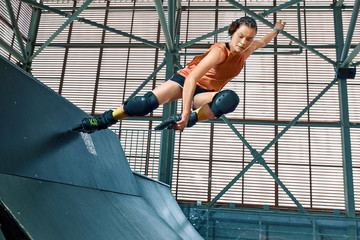 Rollerblader jump high from big air ramp performing trick. Indoors skate park equipment.