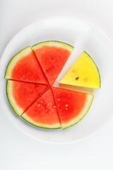 Pieces of red and yellow watermelon in a white round plate, on a white background. View from above. A slice of yellow watermelon is one among the red pieces. Highlight