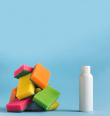 on a blue background there is a white plastic bottle with detergent and cleaning agent and next to it lies a mountain of sponges for washing dishes