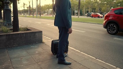 Indian businessman wearing blue suit standing with travel bag or suitcase near office or hotel. Travel business concept
