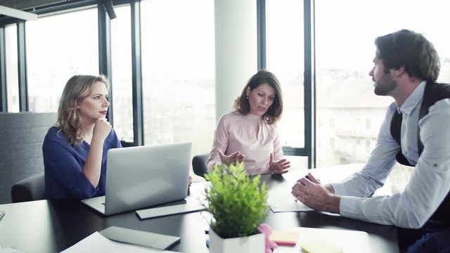 A group of business people with laptop sitting in an office, talking.