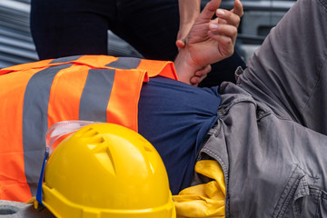 Cropped image of a paramedic's hands checking the pulse rate of a lying down construction worker...