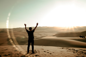 Fototapeta na wymiar young man on sand in a desert near Huacachina, Ica region, Peru. The sunset desert view.
