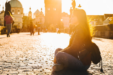 woman sitting on the ground at sunrise at charles bridge in Prague