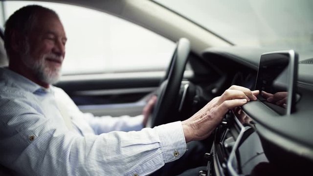 Senior man driver sitting in car, setting radio or navigation. Slow motion.