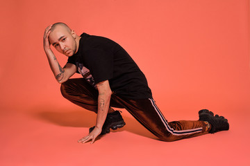Studio shot of a young tattoed bald man posing against a pink background. 90s style.