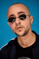 Fototapeta premium Studio shot of a young tattoed bald man posing against a blue background. 90s style.
