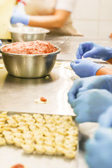 Dumplings manufacturing process. Hands of employers in blue rubber gloves and damplings on tray covered with wax paper.