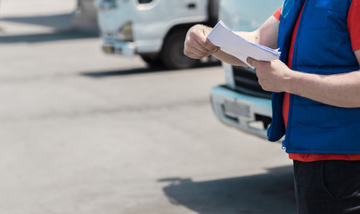 Fototapeta premium Courier driver in uniform making notes in document and delivery white truck behinde him