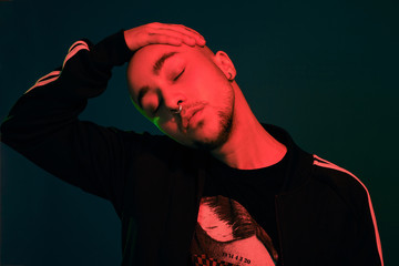 Studio shot of a young tattoed bald man posing against a colorful background. 90s style.