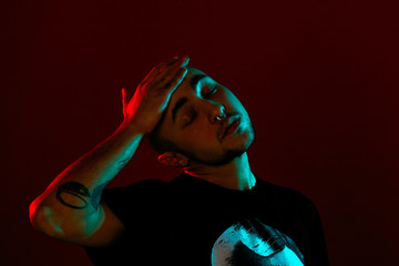 Studio shot of a young tattoed bald man posing against a red background. 90s style.