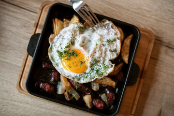 On the pan has a baked tasty dish - potatoes with bacon and smoked sausages and fried egg. Not very useful but a delicious dish. Top view