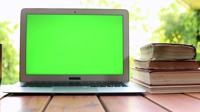 Closeup view of modern laptop with green screen and lots old books on background. Technology development. Online education courses. Freelance lifestyle. Study app. Chroma key display. Sunlight.