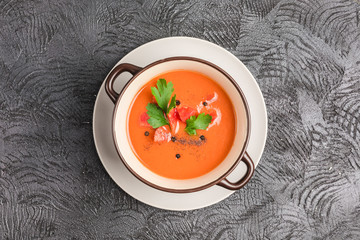 Spanish cold gazpacho soup with tomatoes, pepper, garlic and fresh herbs in a dark plate on black background top view with copyspace