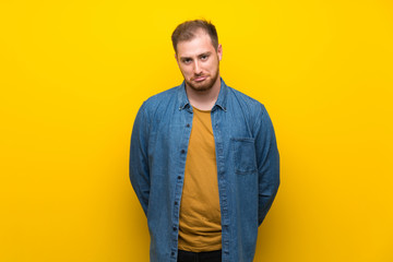 Fototapeta premium Blonde man over isolated yellow wall with sad and depressed expression