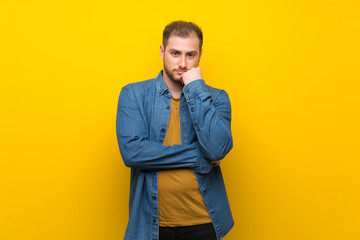 Fototapeta premium Blonde man over isolated yellow wall having doubts