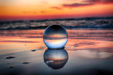 Beautiful sunset on the beach in Slowinski National Park near Leba, Poland. View of a starfish through a glass, crystal ball (lensball) for refraction photography. Wild, untouched nature. - obrazy, fototapety, plakaty