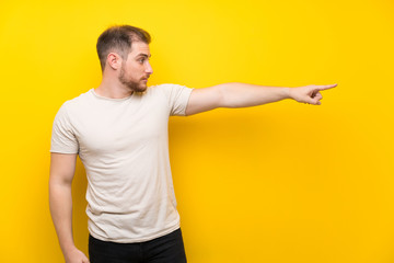 Handsome man over yellow background pointing finger to the side