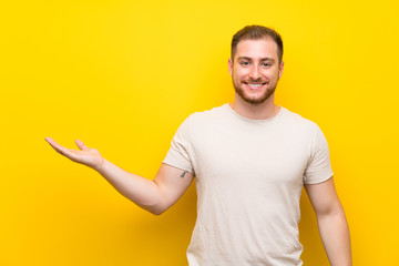 Handsome man over yellow background holding copyspace imaginary on the palm