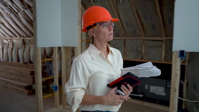 Female construction project manager with hard hat doing walkthrough inspection of new house construction with computer tablet.